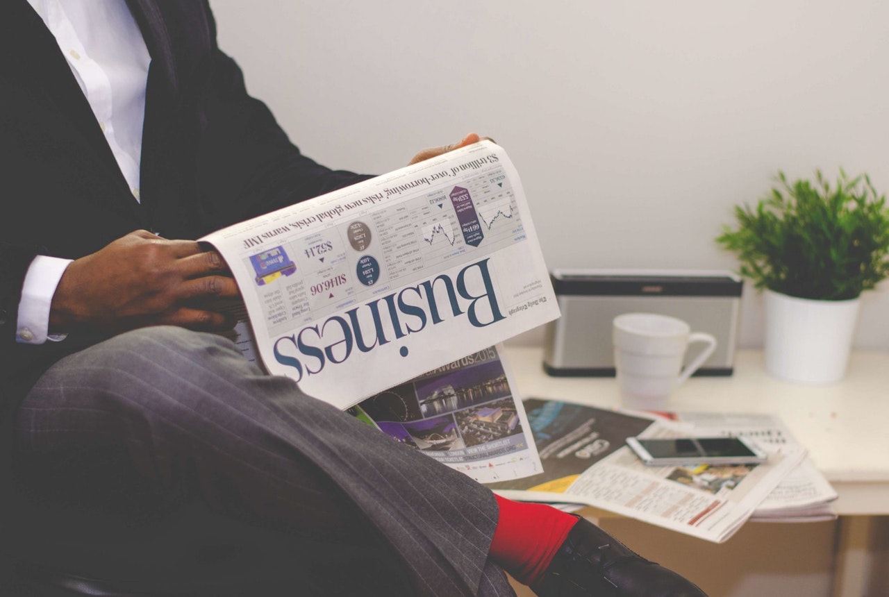 man-reading-newspaper-while-sitting-near-table-with-935979